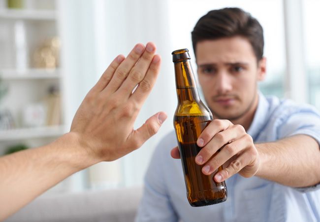 Молодой мужчина в светло-голубой рубашке протягивает бутылку пива навстречу руке, которая решительно отталкивает её